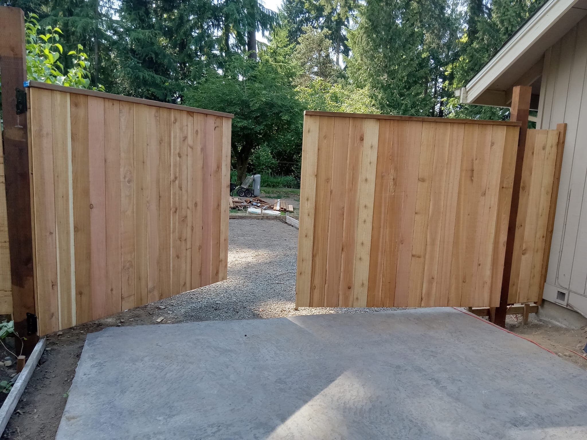 Cedar fence gates fully open showing concrete entry pad and gravel pathway